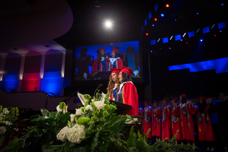 Two female graduates sing at podium