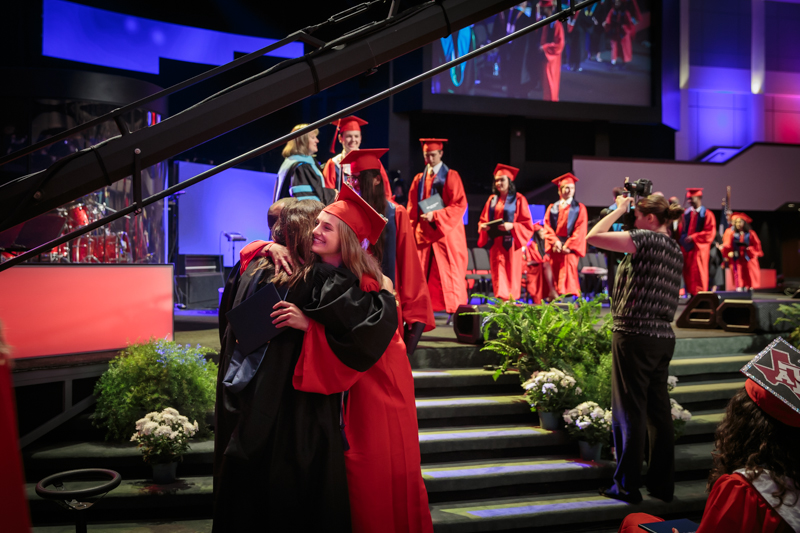 Graduate hugging after walking off stage with diploma
