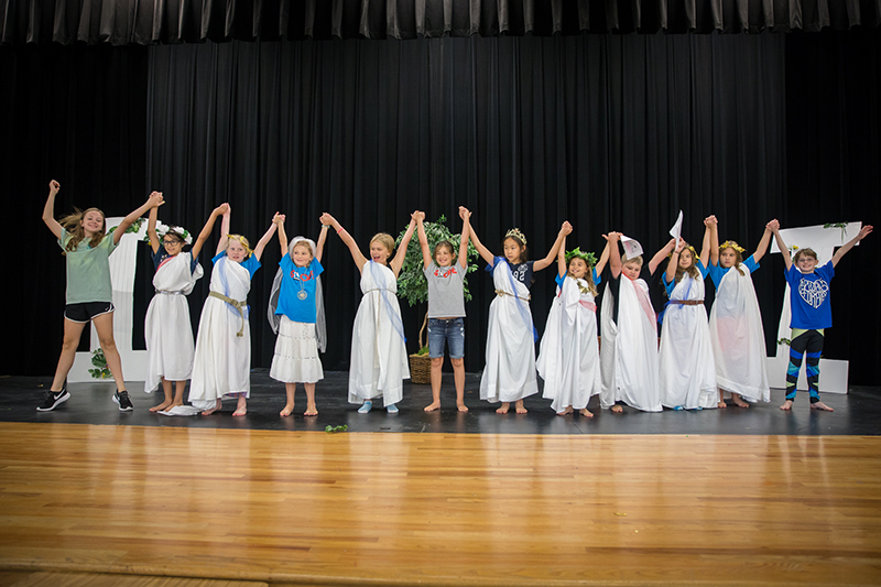Students onstage in Greek costumes raising hands in a line.