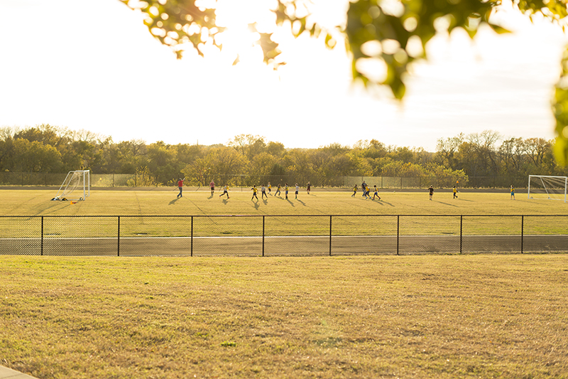 Wide view of soccer field from a distance with students playing soccer o the field