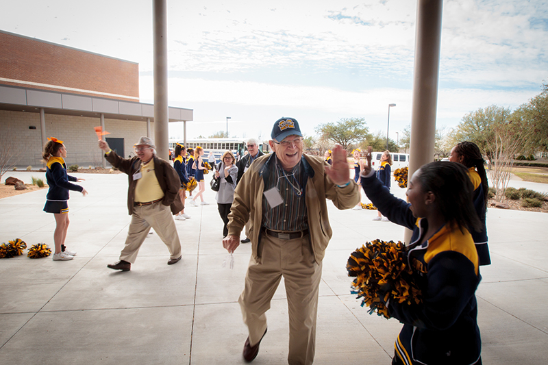 Gentleman from Senior Tour high fiving a Dowell cheerleader in front of the school