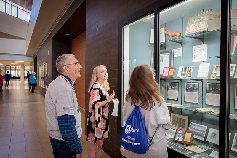 Student and two senior tour members talking in front of display case