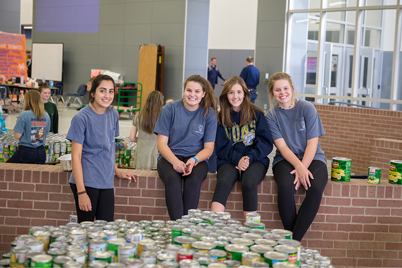Four girls smiling by table with canned goods