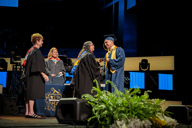 McKinzie handing graduate a diploma and shaking his hand