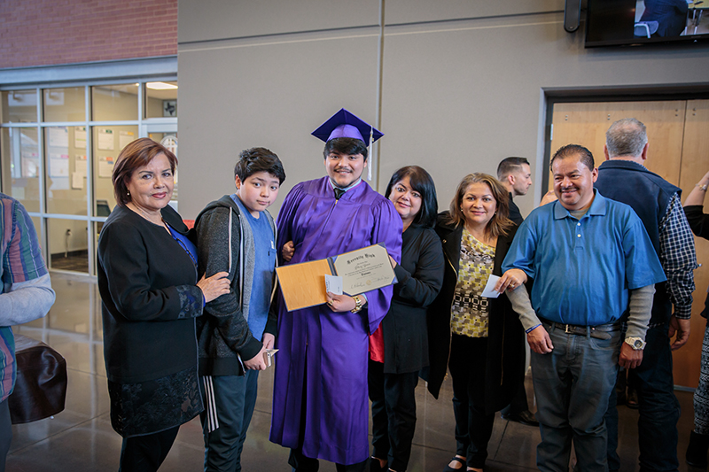 Graduate smiles holding diploma in front of him with family on either side