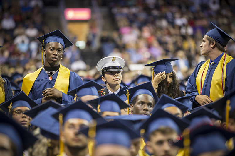 female student in uniform standing among fellow graduates