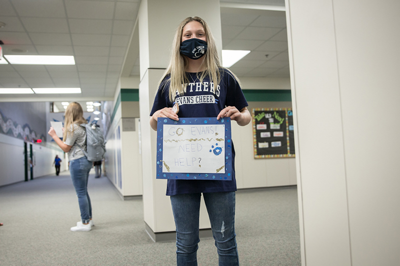 female student wearing mask holding sign in the hall