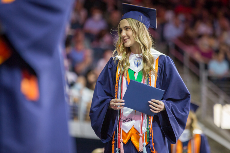 female student walks across stage with diploma