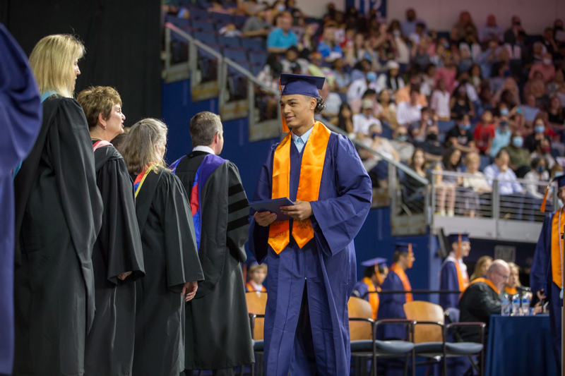 male student with diploma walks across stage