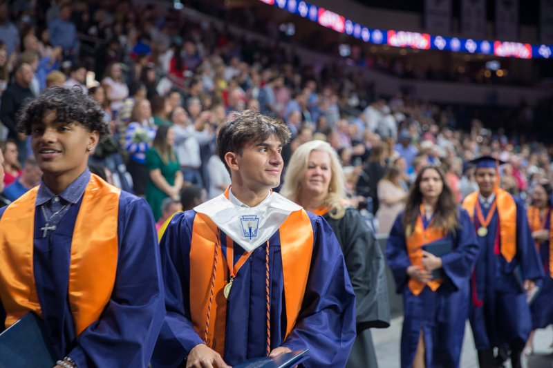 male student smiling as he walks out in a line after ceremony