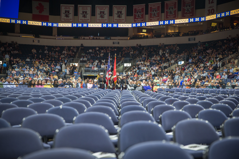 Rows of empty seats with JROTC cadets in background with flags