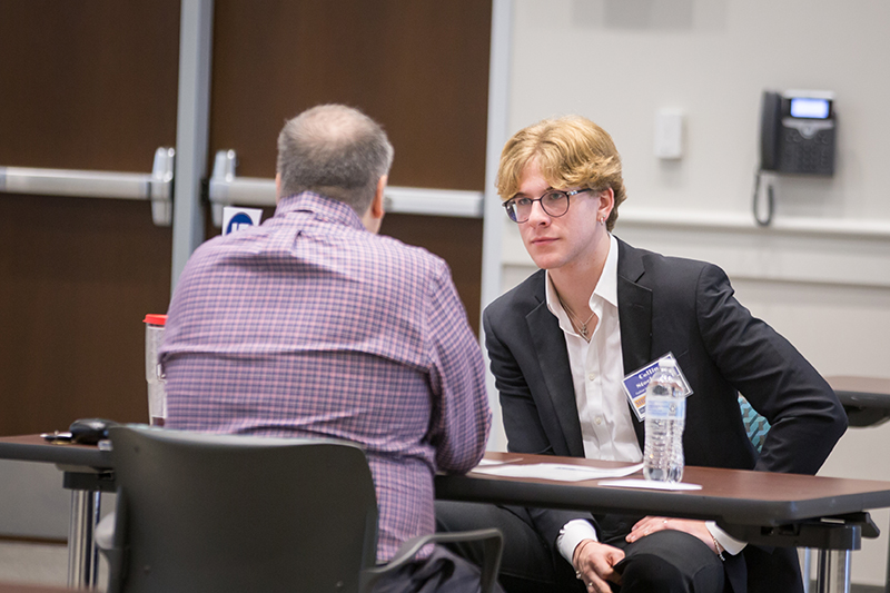 business professional and male student talking at a table