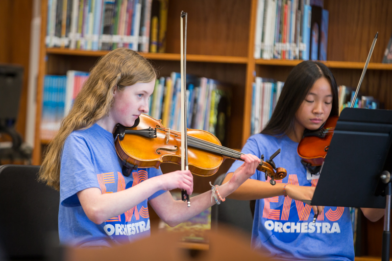two girls in library performing on violins
