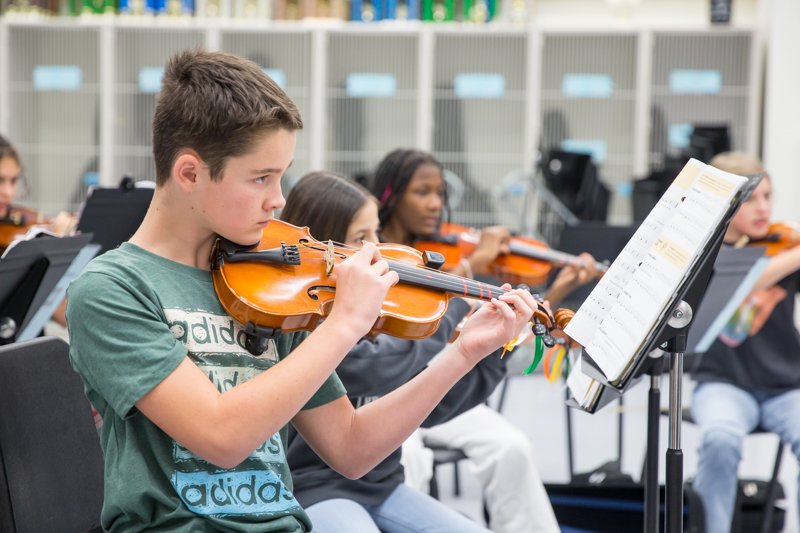 male student plucks his violin strings as he watches director