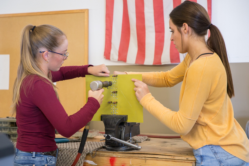 two girls using clamp to hold steel and applying rivets