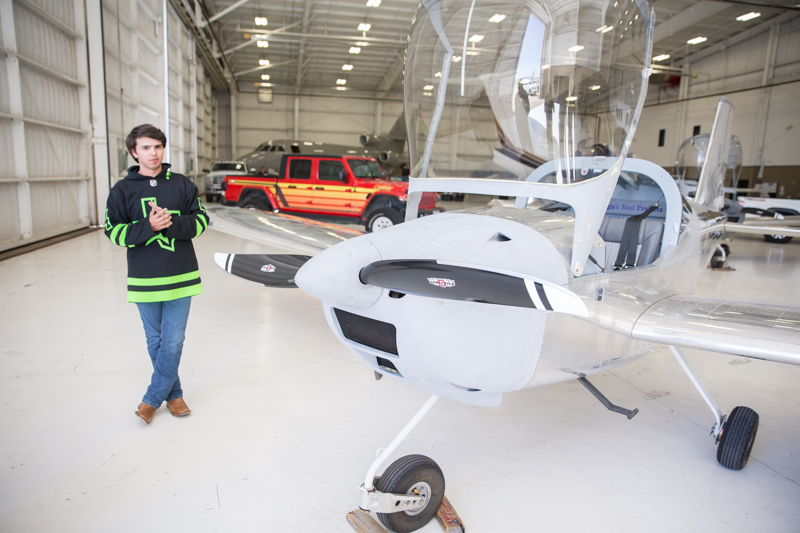 student standing next to the plane in the hangar