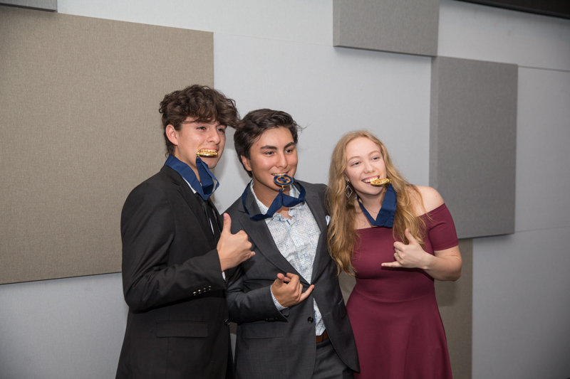 three students biting awards while giving thumbs up