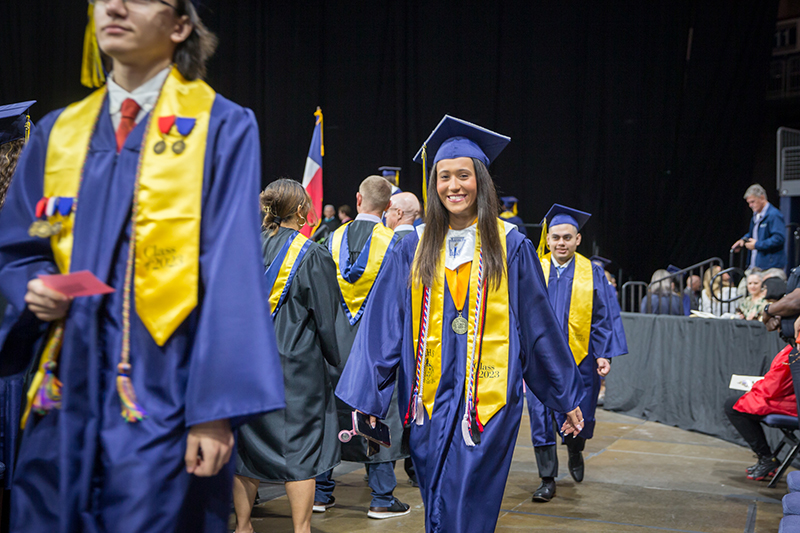 line of graduates walking in, female student smiling at camera