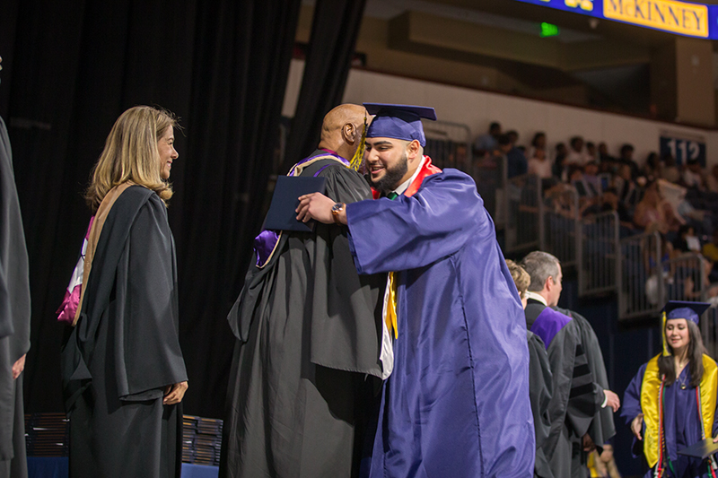 male graduate hugging board member Larry Jagours on stage as he goes down line