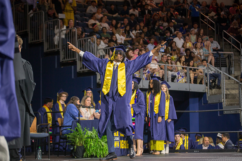 male MHS student with arms spread wide and up as he walks across stage