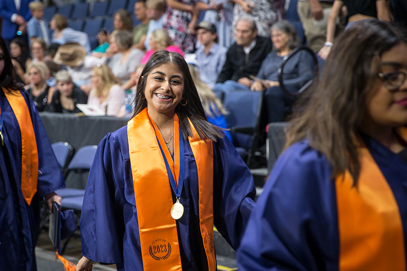 female North student walking out in a line and smiling at camera after ceremony