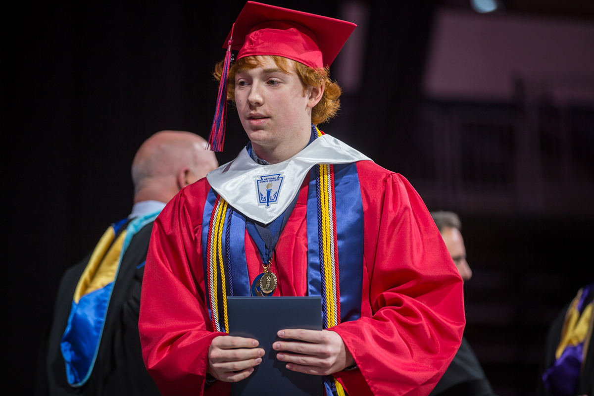 male student walking across the stage holding his diploma 