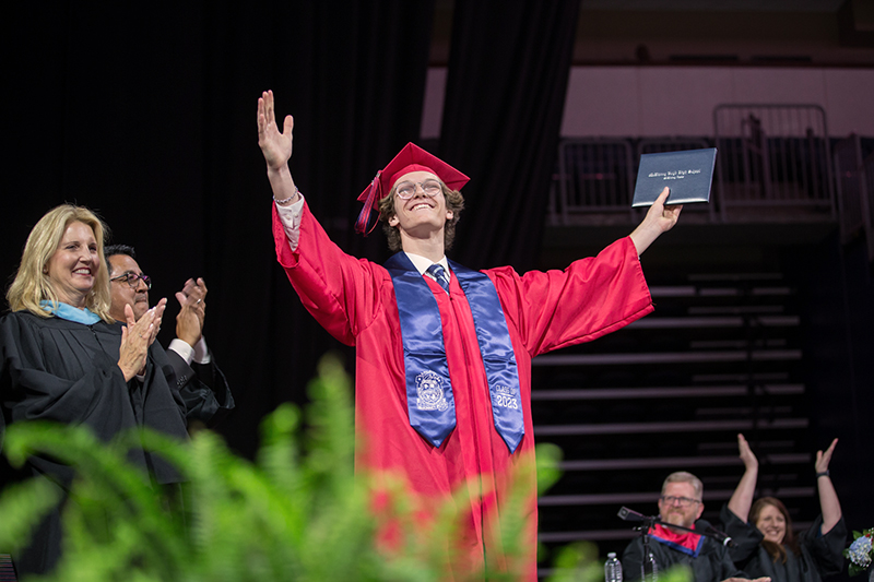 final boyd graduate with hands raised toward the audience as everyone claps
