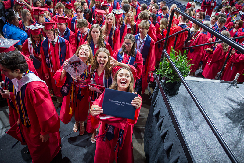 3 joyous female Boyd graduates holding up diplomas and cap with Texas Tech logo on it as they leave
