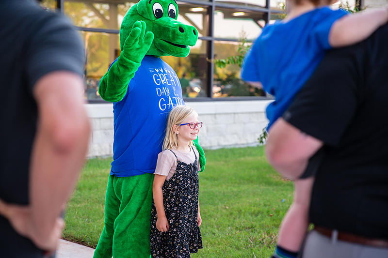 smiling young girl posing with gator mascot for a photo as parents look on