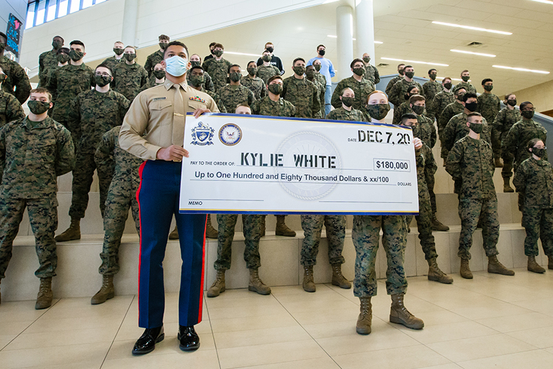 Kylie holding check with Marine with battalion in the background.