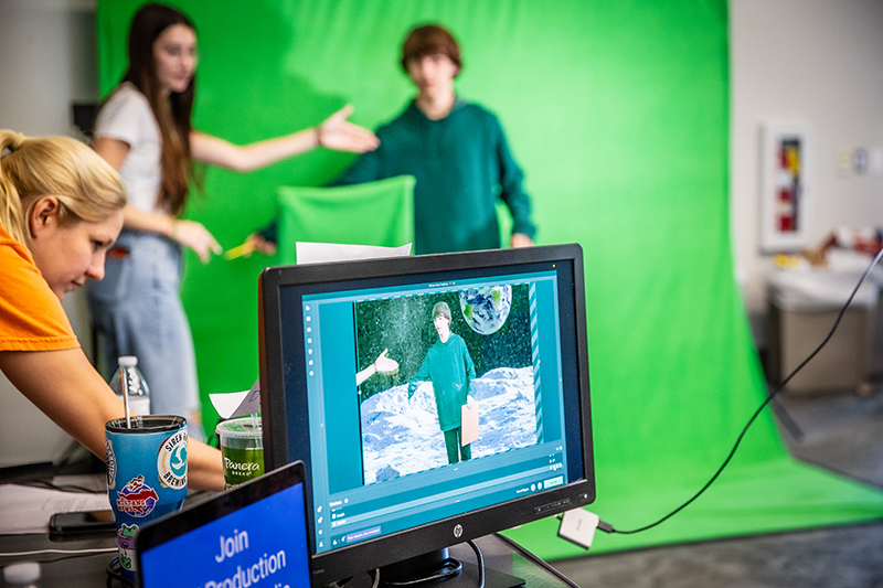 students in background in front of green screen with computer image in foreground showing them on the moon