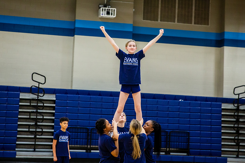 cheerleader on top of pyramid with arms raised