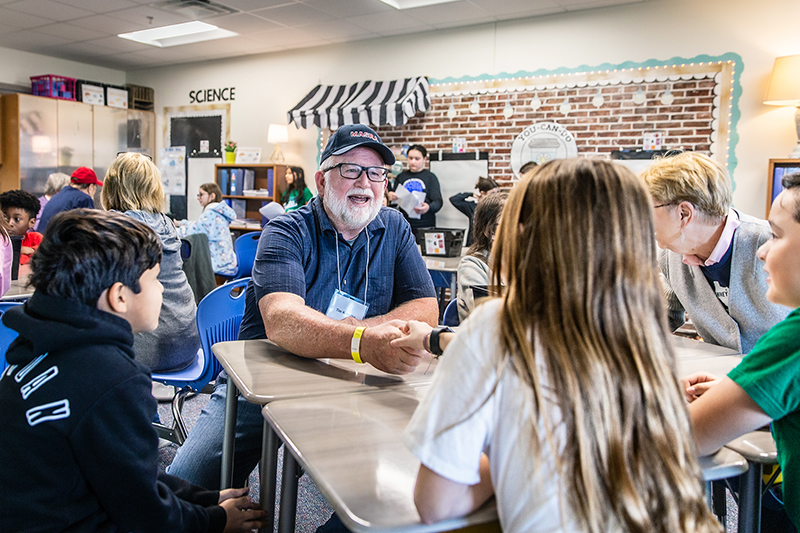 man on tour sitting at table with students shaking student's hand 