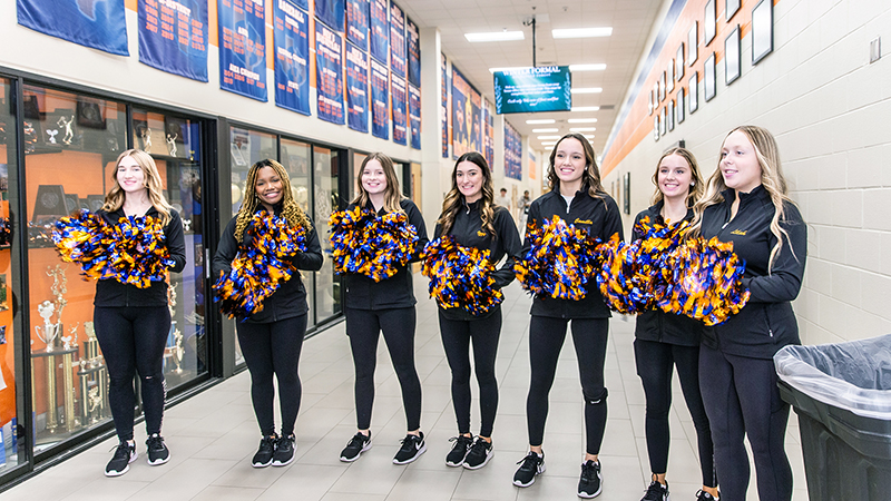 members of the drill team lined up across the hall holding pom poms to welcome guests